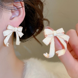 Close-up of cream bow earrings with rose gold trim showing enamel texture and detail