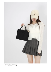 Detail of a minimalist black canvas tote bag with a practical front pocket and twin handles
