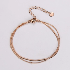 Close-up of rose gold double-layer snake chain bracelet with beads and heart charm