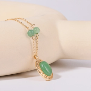 Dettaglio del ciondolo con gemma verde ovale e perline su una collana dorata