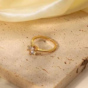 Detail of an 18K gold plated ring with a round clear zircon set on a beige stone surface