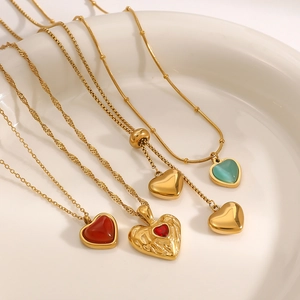 Gold heart pendant necklaces with red agate and green cat eye stones on a white tray
