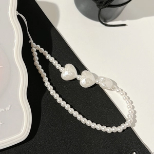 Detail view of pearl phone strap featuring white heart beads on a minimalist background