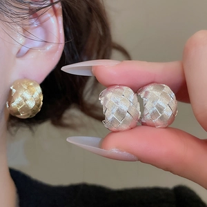 Close-up of C-shaped metal earrings with intricate woven texture in gold and silver