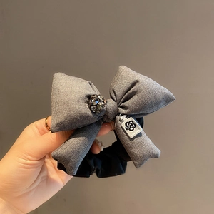 Detailed shot of grey tweed bow scrunchie with rhinestone center and camellia charm