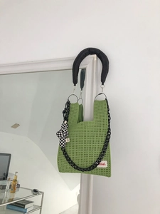 Detail of green knitted tote bag with chunky black handle and chic checkerboard charm