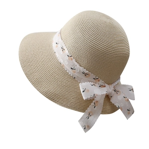 Detailed macro view of the beige woven straw hat featuring a floral print ribbon bow