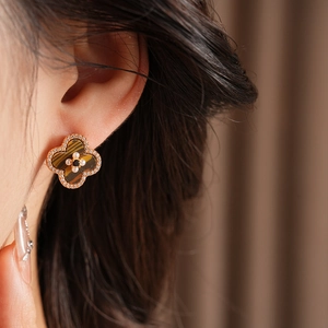Detailed close-up of a golden clover earring with pearls and zircon inlays on a model