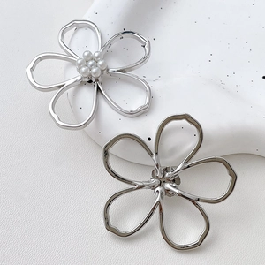 Detail of silver hollow flower earrings with white pearl centers on a textured stone tray