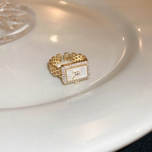 Nahaufnahme eines goldenen Rings im Uhrenstil mit Zirkonia auf Keramiktablett