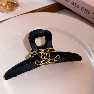 Detail of matte black hair claw clip with golden chain weave CC logo on white plate