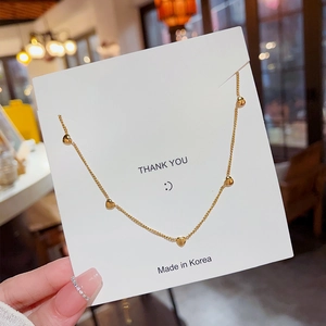Elegant gold chain necklace featuring five heart charms displayed on a card