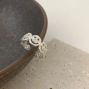 Macro shot of silver textured ring featuring repeating smile faces and open-loop design