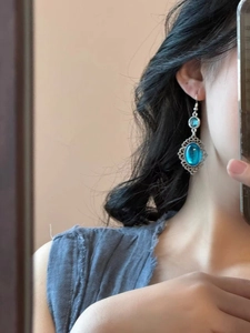 Close-up of vintage silver earrings with oval sea blue resin stone worn by a model