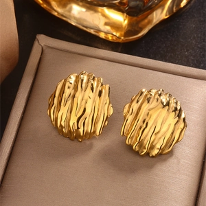 Close-up of golden round stud earrings with irregular wave texture on a brown display mat
