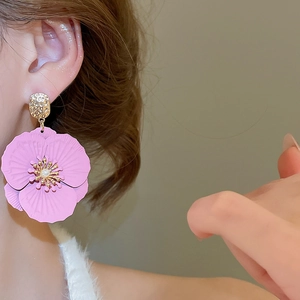 Détail de boucles d'oreilles fleur rose avec accents dorés portées par un mannequin