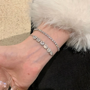 Gros plan de bracelets argentés superposés avec zircon carré et rond sur un poignet
