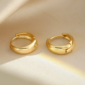 Macro shot of minimalist polished gold hoop earrings resting on smooth silk fabric