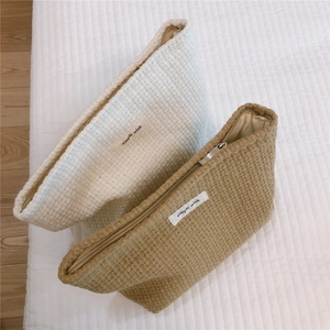 Close-up detail of coarse woven grid makeup bags in cream and light camel color