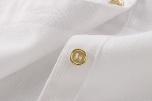 Close-up of white linen shirt fabric featuring elegant gold buttons and textured weave