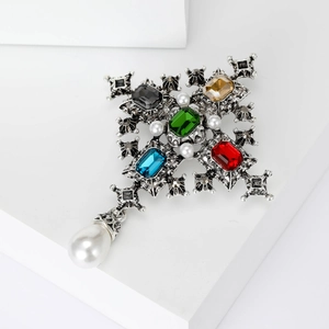 Baroque cross brooch with colorful gemstones and hanging pearl drop on white background