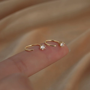 Minimalist gold hook earrings with round six-prong crystals shown on fingertips