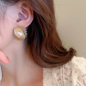 Close-up of elegant gold spiral stud earrings with white pearl accent worn by a model