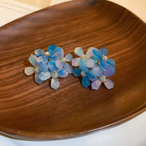 Detail of gradient blue-purple resin flower earrings with pearls on a wooden tray