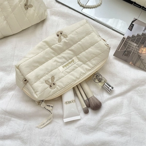 Close-up of quilted cream makeup bag with brown bunny embroidery and ribbon zipper pull