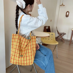 Detail of yellow checkered canvas tote bag with metal logo and long shoulder handles
