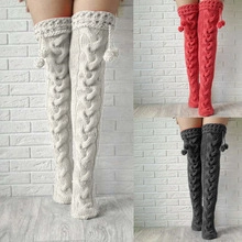 Detail of cable knit over-knee socks with decorative pom-poms in cream, red, and grey