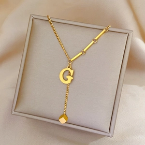 Gold titanium steel necklace featuring letter G and cube pendants on a jewelry box