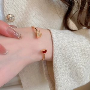 Close-up of gold open cuff bracelet with zircon butterfly and red heart on female wrist