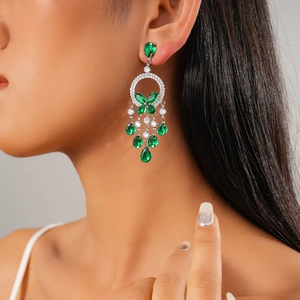 Close-up of model wearing luxury silver butterfly earrings with emerald green teardrop gems