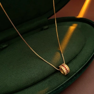 Macro detail of a gold cylinder necklace pendant with red zircons in a green velvet box