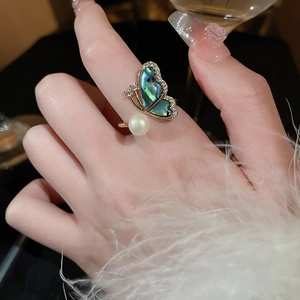 Macro detail of gold-plated butterfly ring featuring abalone shell and pearl on finger