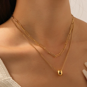 Double-layered gold necklace featuring paperclip chain and round bead pendant on model