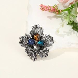 Vintage silver flower brooch with colorful crystals on a textured white stone base