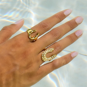 18K gold horseshoe open rings with white diamonds on hand over water ripples