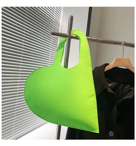 Close-up of heart-shaped felt handbag in neon green hanging on a metal rack