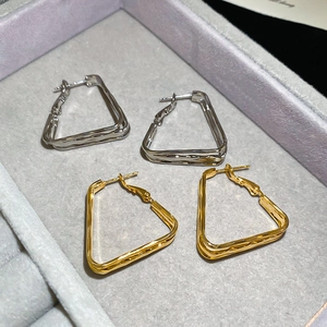 Macro detail of textured 18k gold and silver geometric hoop earrings on velvet tray