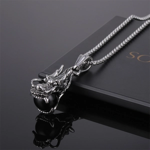 Détail du pendentif dragon argenté avec perle noire sur une chaîne robuste et reflet