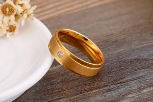 Dettaglio anello in acciaio dorato spazzolato con diamante su ceramica bianca