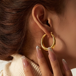 Close-up of chunky gold hoop earrings in polished stainless steel on a female model