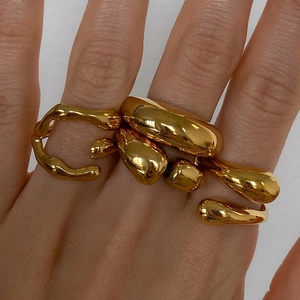 Irregular chunky gold rings with lava texture on female hand against gray backdrop
