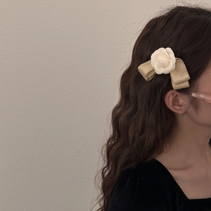 Elegant camellia bow hair clip with champagne satin ribbon on brown wavy hair