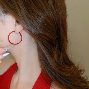 Close-up of minimalist large red hoop earrings worn by a model in a red knit sweater