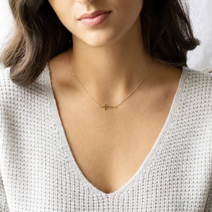 Detail of a minimalist gold stainless steel necklace with a side-mounted cross pendant