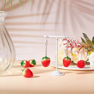 Detail of red resin strawberry charms on white earring display with soft shadows