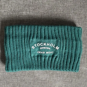 Makro-Detail des dunkelgrünen Strickstirnbands mit weiß geprägtem Stockholm-Sweden-Text